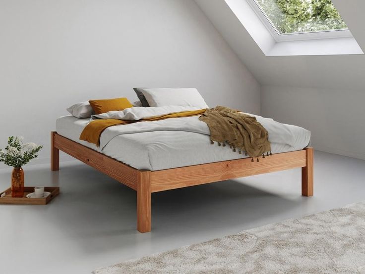 a bed sitting in the middle of a room under a skylight next to a potted plant