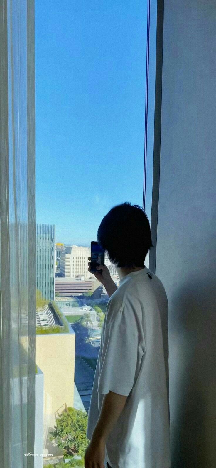 a man standing next to a window looking out at the cityscape and water