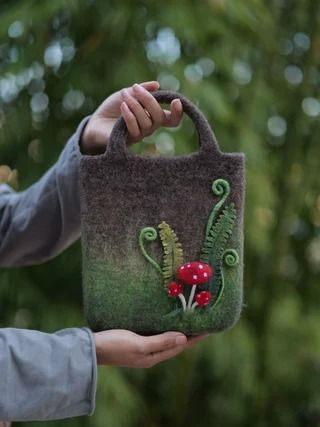 a woman is holding a bag with flowers and plants painted on it in front of some trees