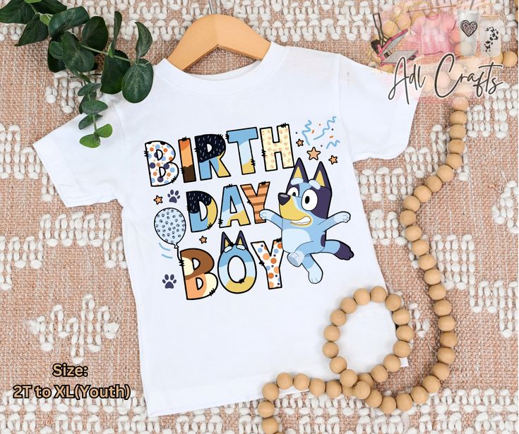 a white shirt with the words birth day boy printed on it next to a wooden bead necklace