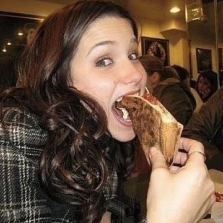 a woman is eating a hot dog at a restaurant with her mouth open and tongue out