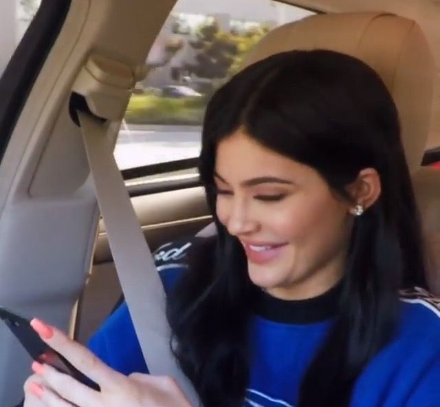 a woman sitting in the back seat of a car looking at her cell phone and smiling