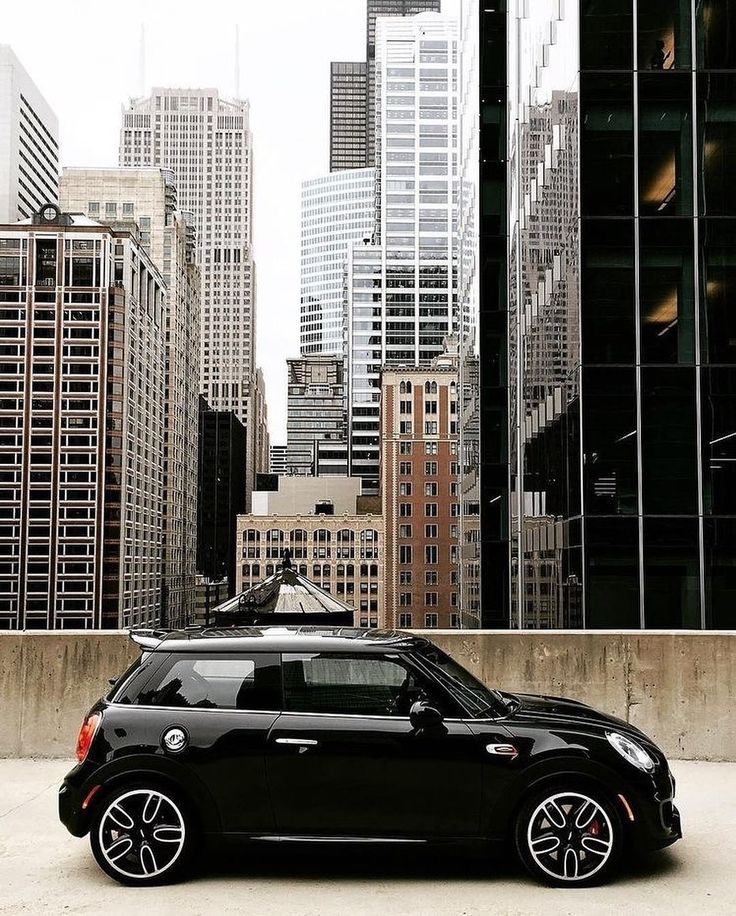 a small black car parked in front of tall buildings with skyscrapers in the background