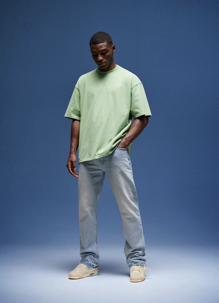 a man standing in front of a blue background wearing a green t - shirt and jeans