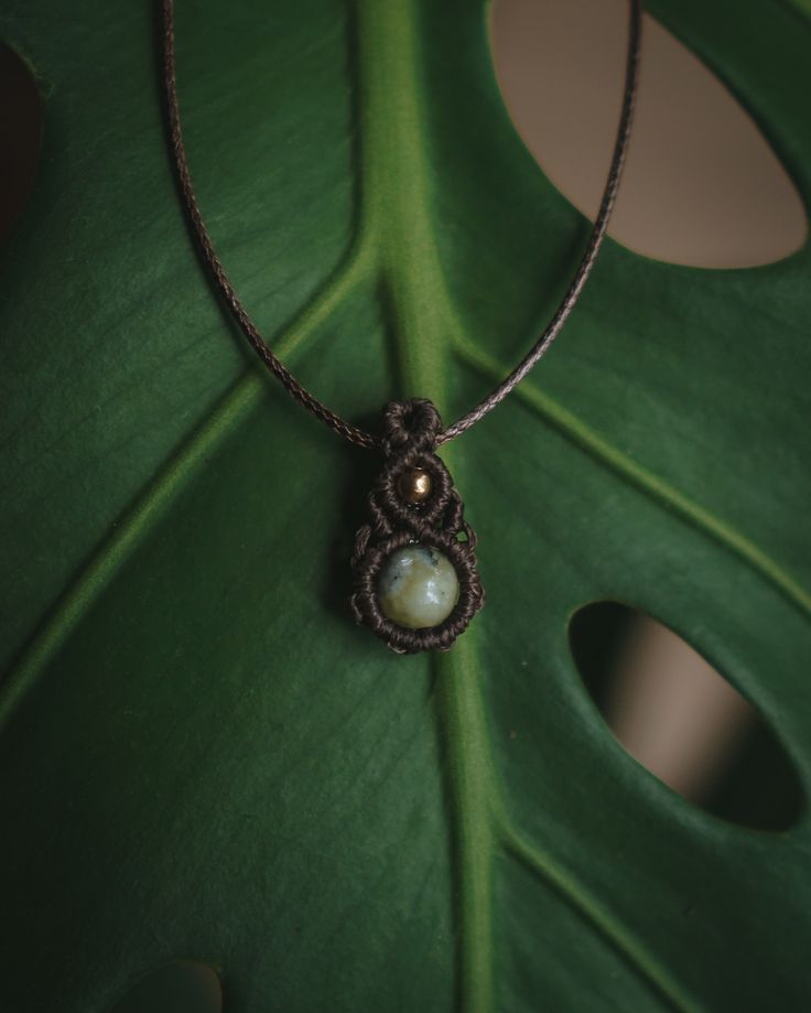 a close up of a green leaf with a necklace on it's end and two pearls in the middle