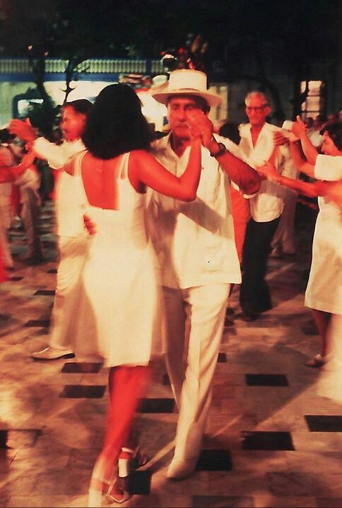 a man and woman dancing on the dance floor with other people in white dresses behind them