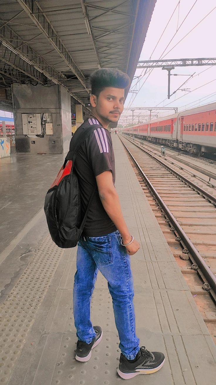 a young man is standing on the train platform with his back to the camera and looking at the camera