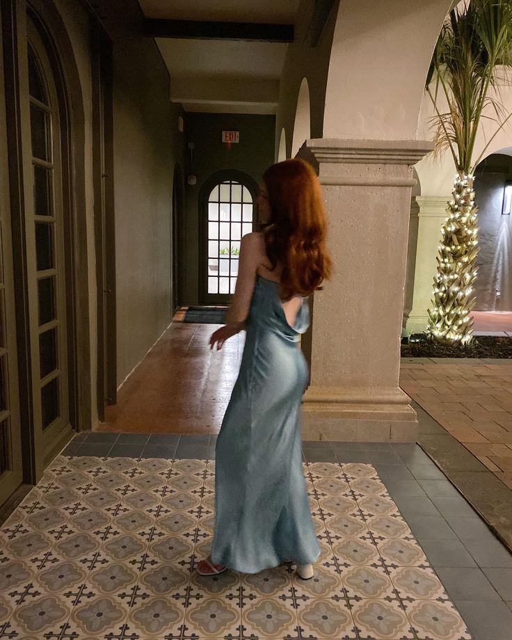 a woman in a blue dress is standing on a tile floor and looking at something