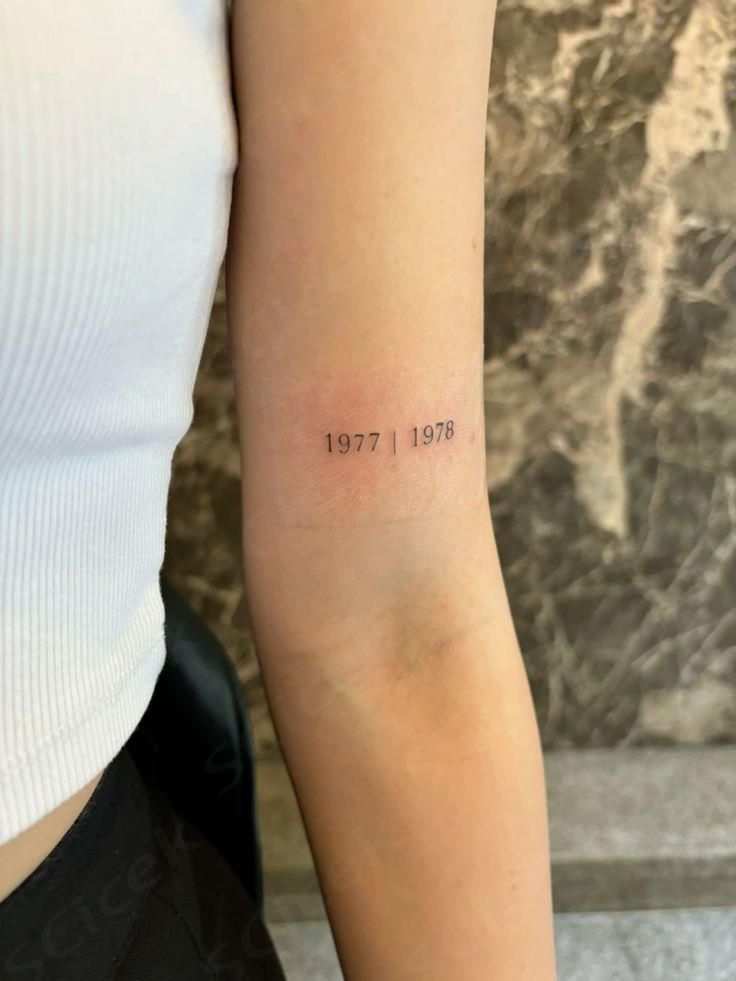 a woman with a small tattoo on her arm that reads, 1917 - 1971 in cursive font