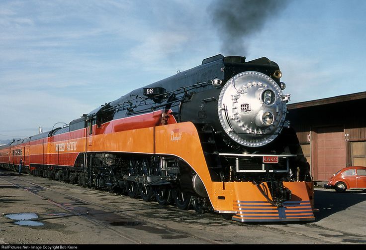 an orange and black train traveling past a building