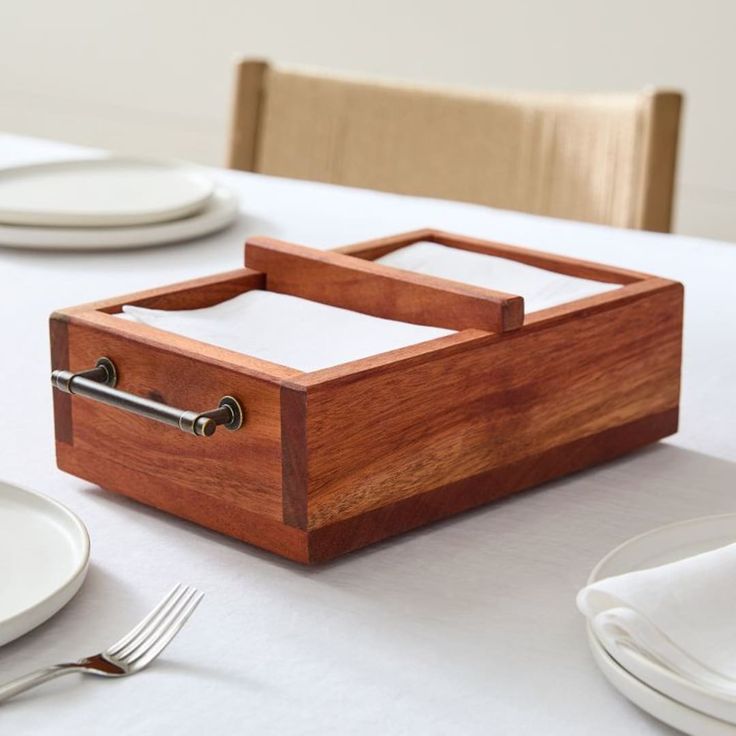 a wooden box sitting on top of a table next to white plates and silverware