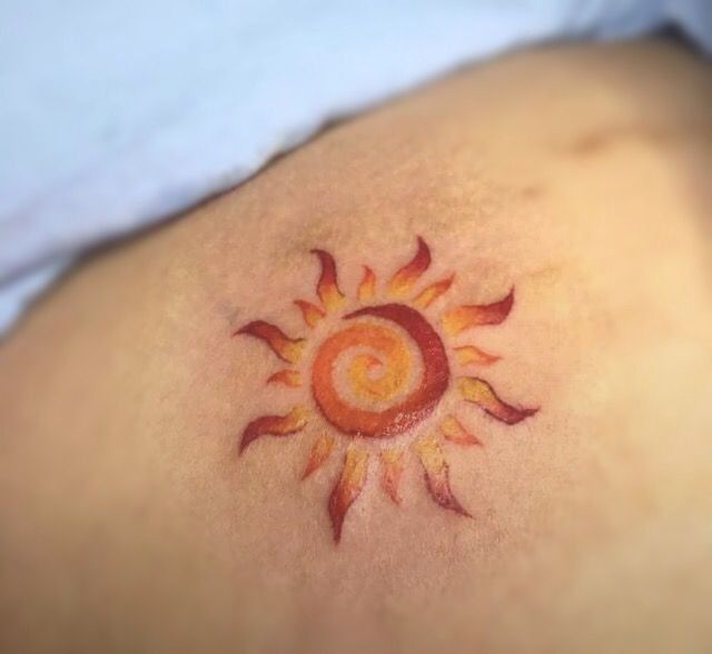 a sun tattoo on the back of a woman's stomach, with red and yellow colors