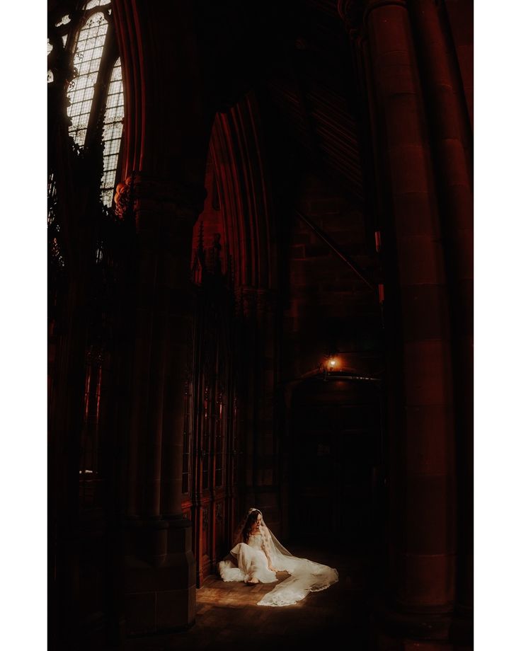 a bride sitting in the middle of an old cathedral with her veil blowing in the wind