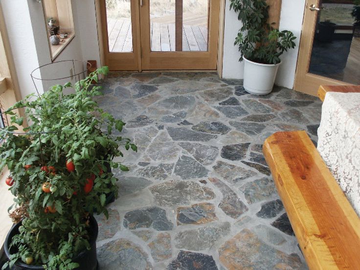 a stone floor with potted plants in front of it and a wooden bench on the other side