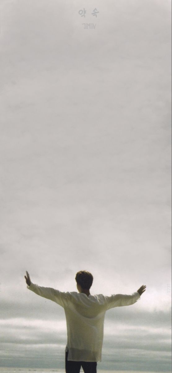 a man standing on the beach with his arms wide open in front of an overcast sky