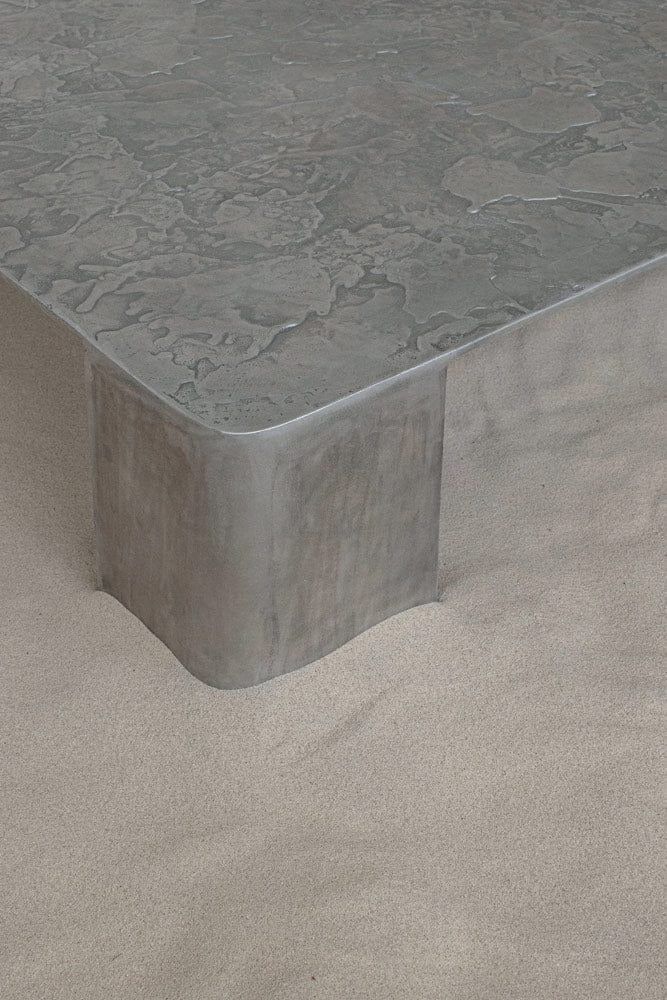 a square concrete table sitting on top of a sandy beach next to the ocean or sea