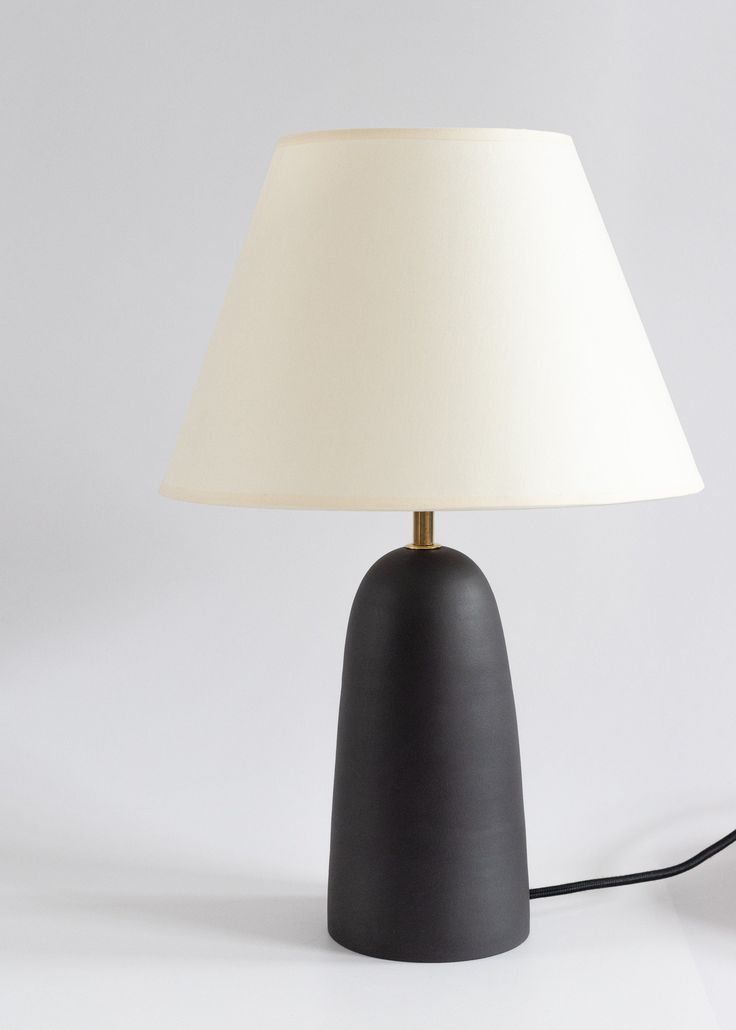 a black table lamp with a white shade on the base and a cord attached to it