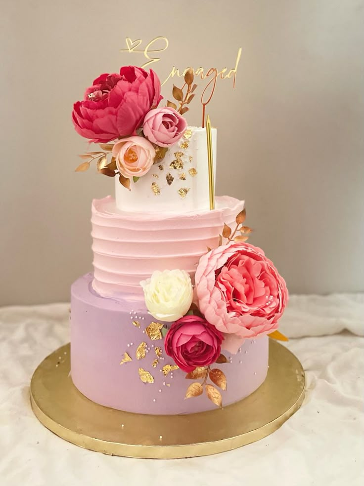 a three tiered cake with pink and purple flowers on top, gold plated serving platter