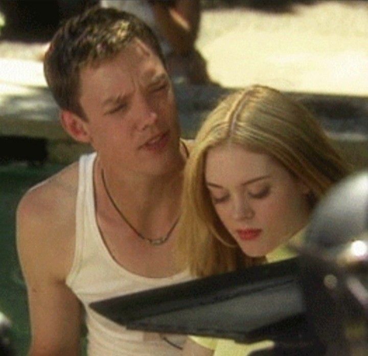 a young man and woman sitting next to each other looking at something on the ground