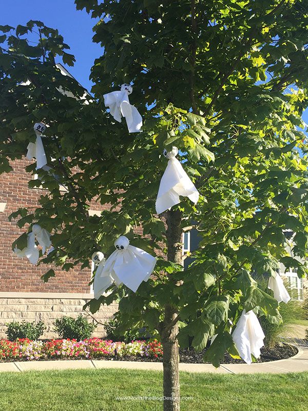 some white paper bags hanging from a tree in front of a brick building with flowers