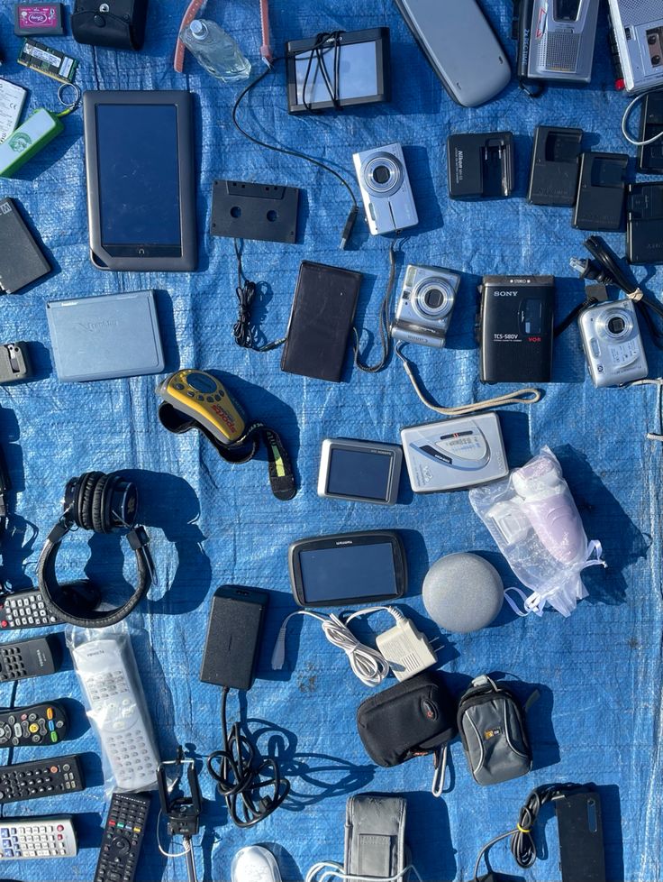 there are many electronic devices on the blue blanketed tablecloth, including cell phones and other electronics