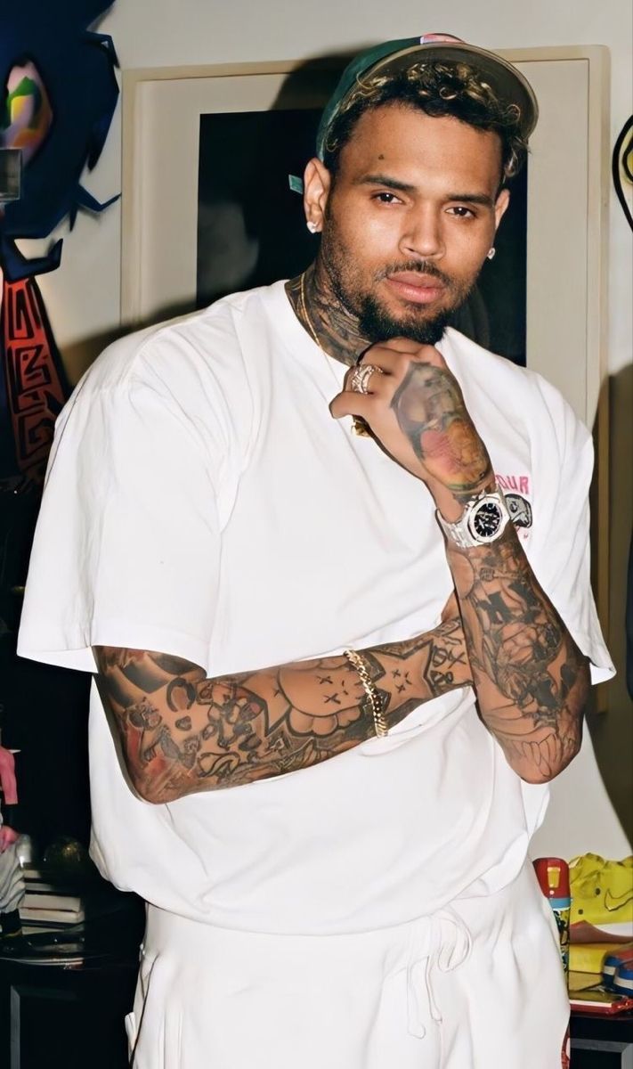 a man with tattoos on his arms and arm is standing in front of a wall