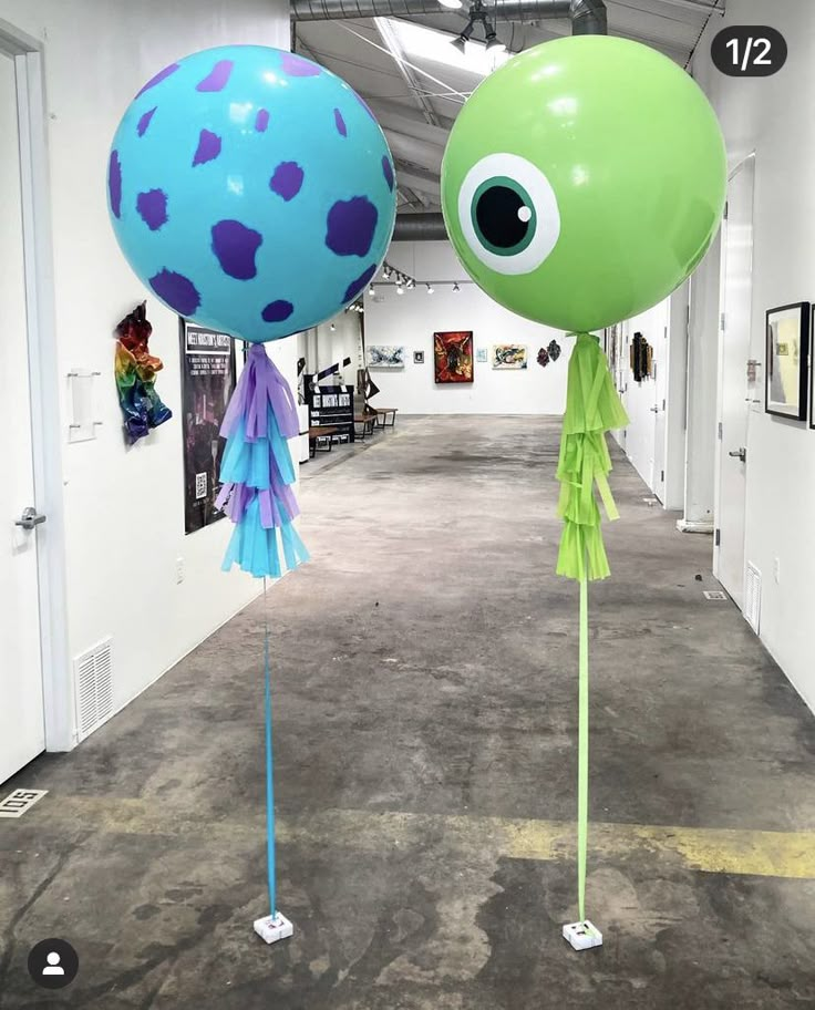 two large balloons with blue and green designs on them in an art gallery, one is shaped like a monster