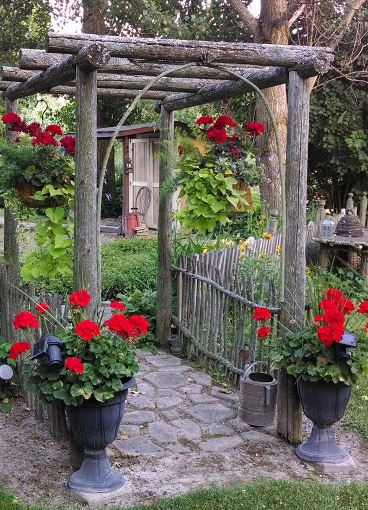 an outdoor garden with potted flowers on the ground and a wooden arbor in the background