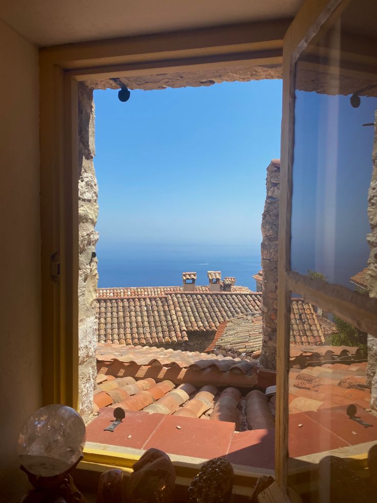 an open window looking out at the ocean from inside a house with red tile roofing