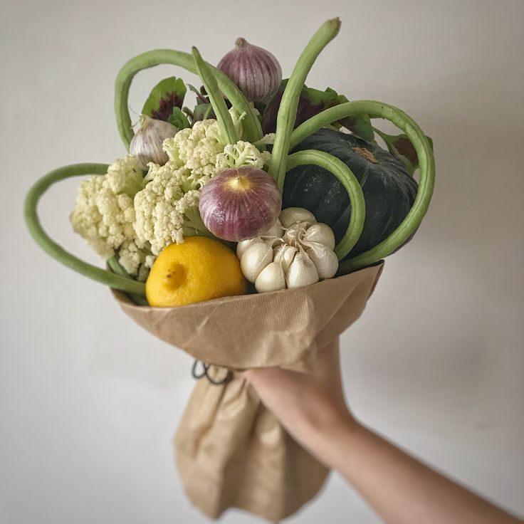 a person holding a bouquet of vegetables and fruit in their hand with a cloth bag