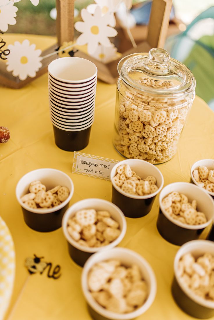 a table topped with lots of cups filled with food next to a jar of cereal