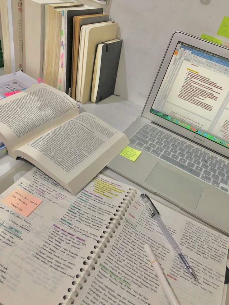 an open laptop computer sitting on top of a desk next to books and notebooks