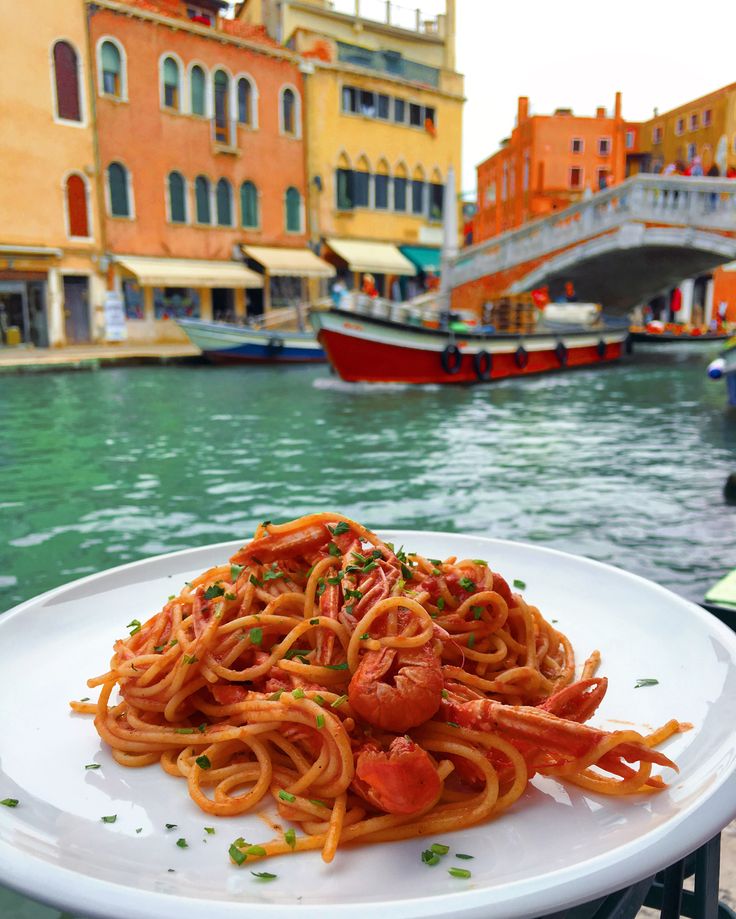 a white plate topped with spaghetti next to a body of water and buildings in the background