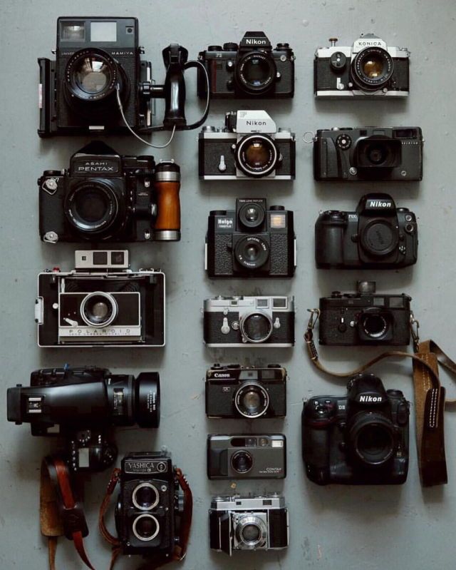 many different types of cameras sitting on top of a table with one camera attached to the wall