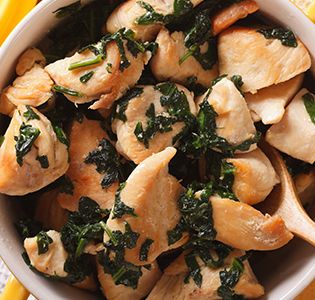 a white bowl filled with chicken and spinach on top of a yellow table cloth