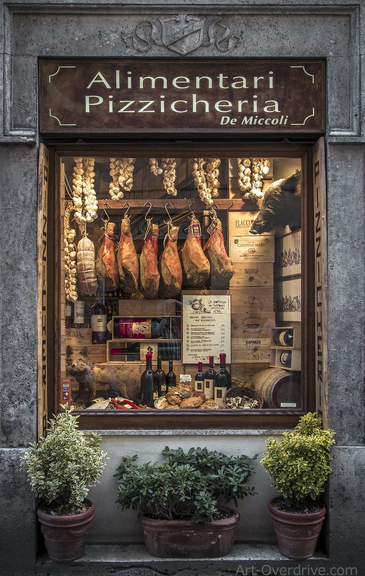 an italian restaurant with meats and vegetables in the front window, surrounded by potted plants