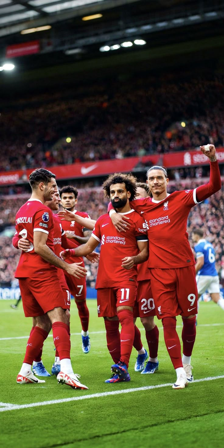 a group of men in red uniforms standing on top of a soccer field with their arms around each other