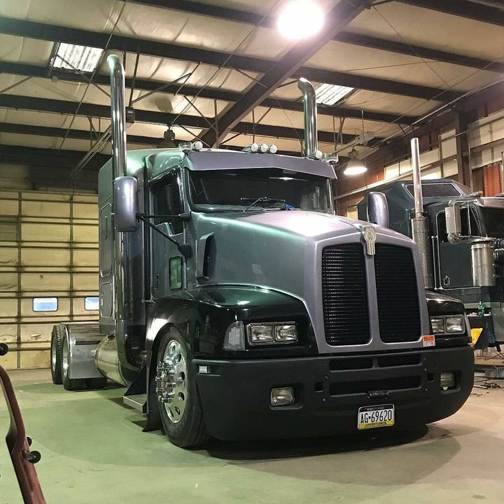 a large semi truck parked in a garage next to another semi truck with its lights on