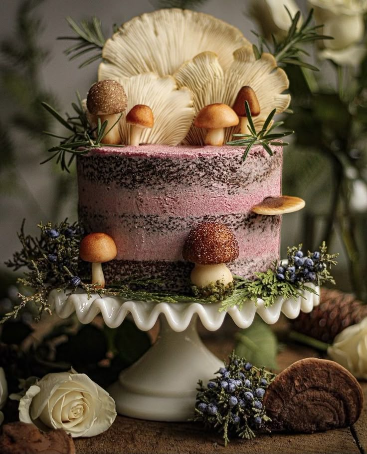 a pink cake with mushrooms and greenery on top sits on a table next to flowers