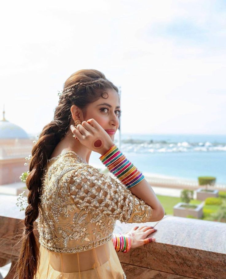 a beautiful young woman standing on top of a balcony next to the ocean with her hands in her hair