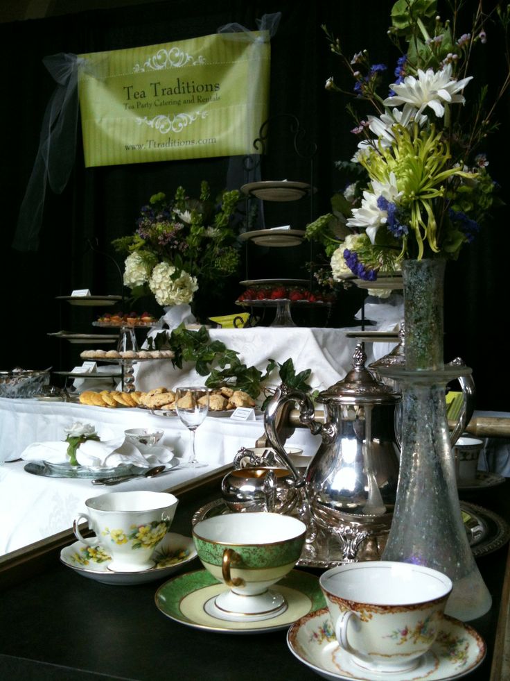 there are many tea cups and saucers on the table with flowers in vases