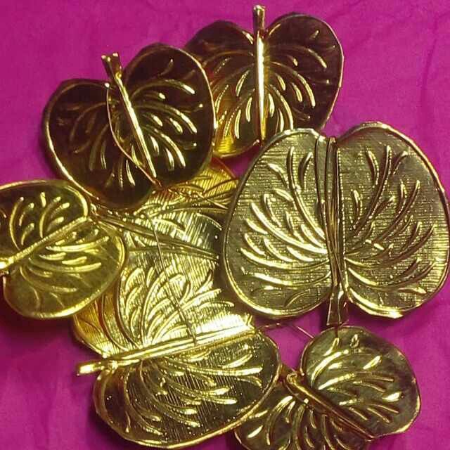 gold plated leaf shaped brooches are on a pink surface with purple background