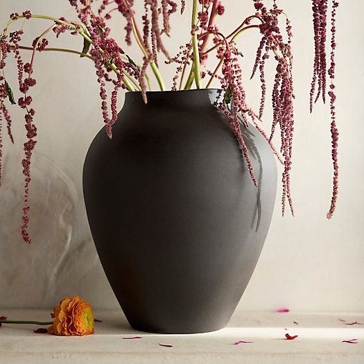 a black vase with pink flowers in it on a table next to a white wall