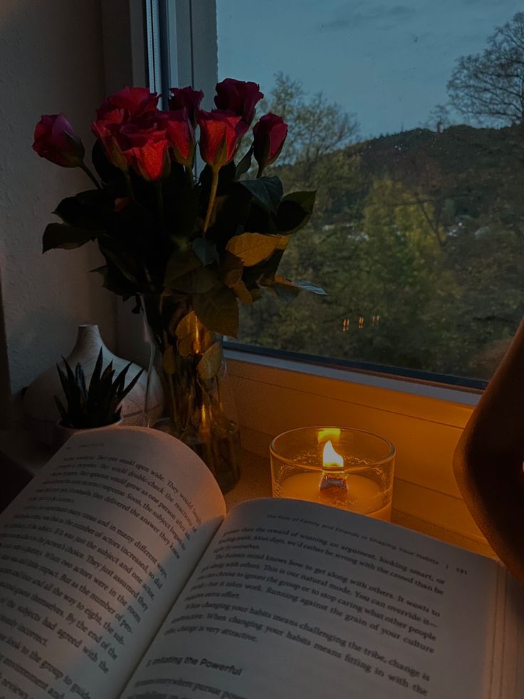 an open book sitting on top of a table next to a vase filled with roses