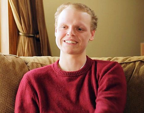 a man in a red sweater is sitting on a couch and smiling at the camera