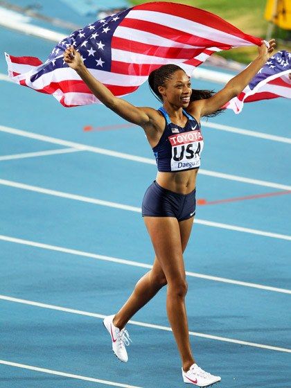 a woman holding an american flag on top of a race track with her arms in the air