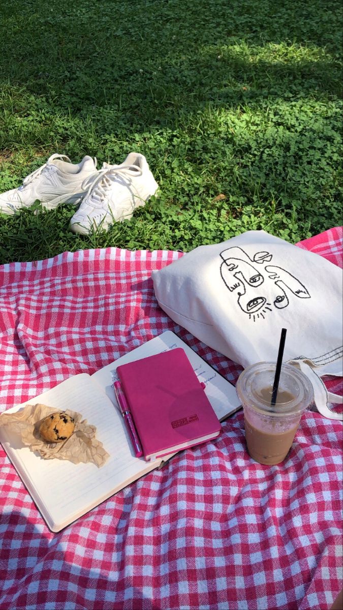 an open book on a picnic blanket next to a cup of coffee and notebooks