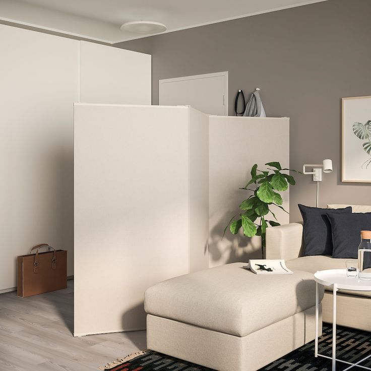 a living room filled with furniture and a plant on top of a white ottoman next to a wall