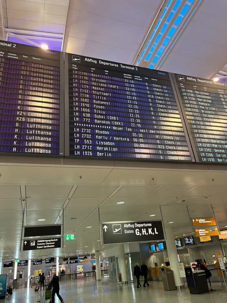 people are walking through an airport terminal with their luggage and check - in boards on the ceiling