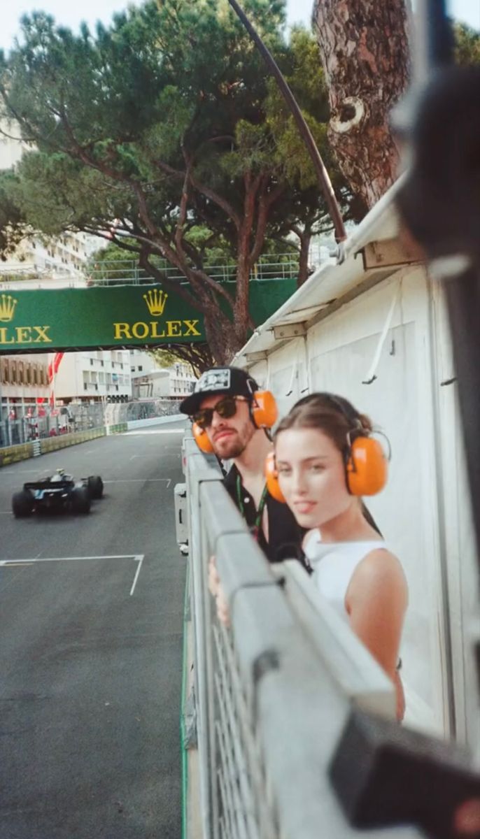 two people wearing headphones are looking out the side of a fence at a race car